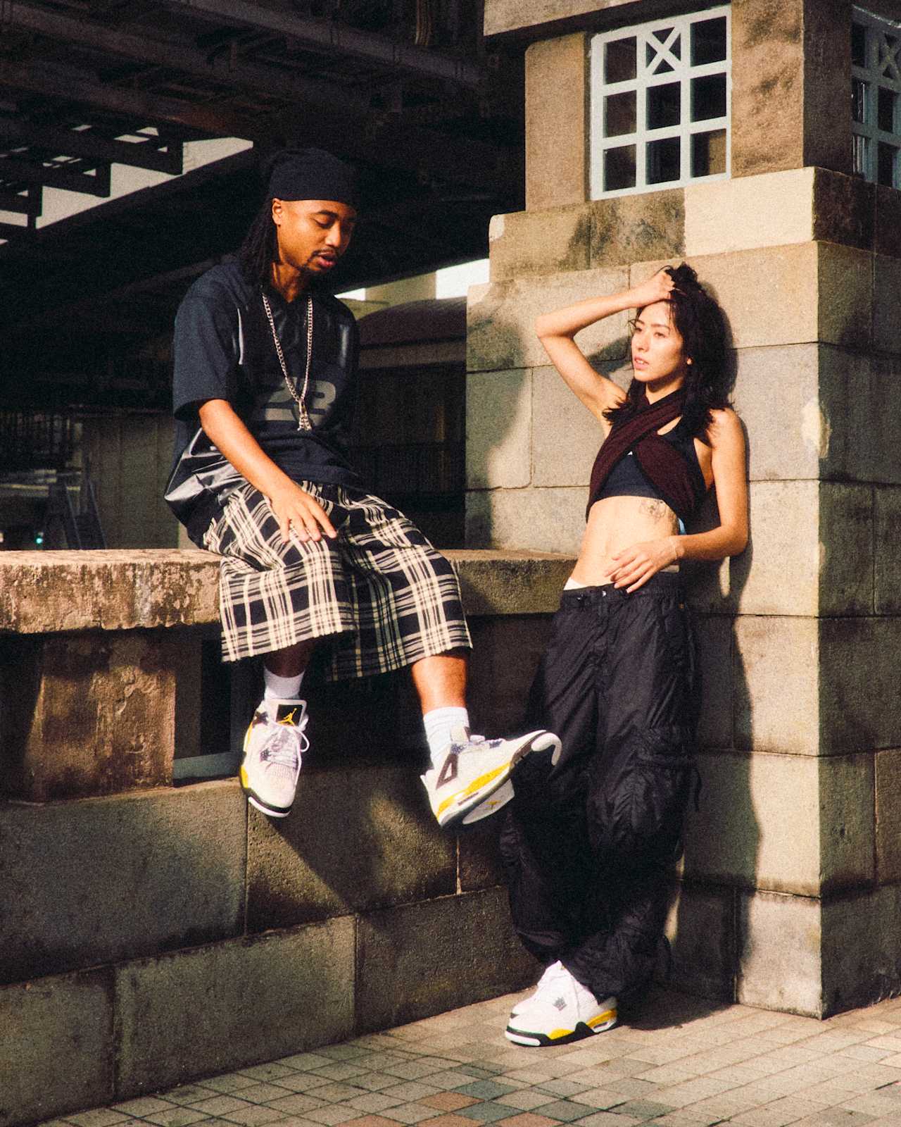 Twee mensen dragen de Air Jordan 4 Tour Yellow op een brug, campagnebeeld