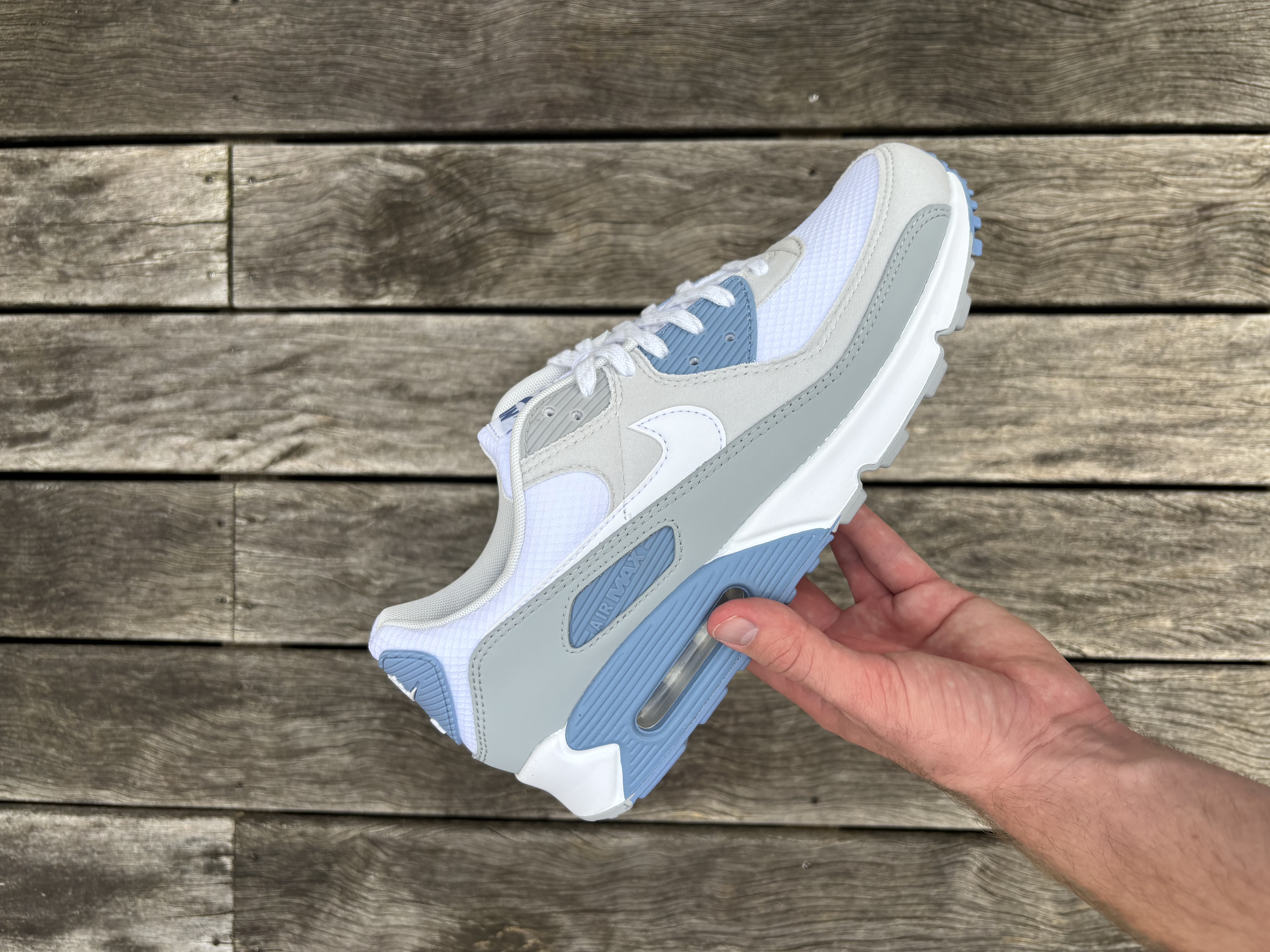 Nike Air Max 90 in wit, grijs en blauw – zijaanzicht in de hand