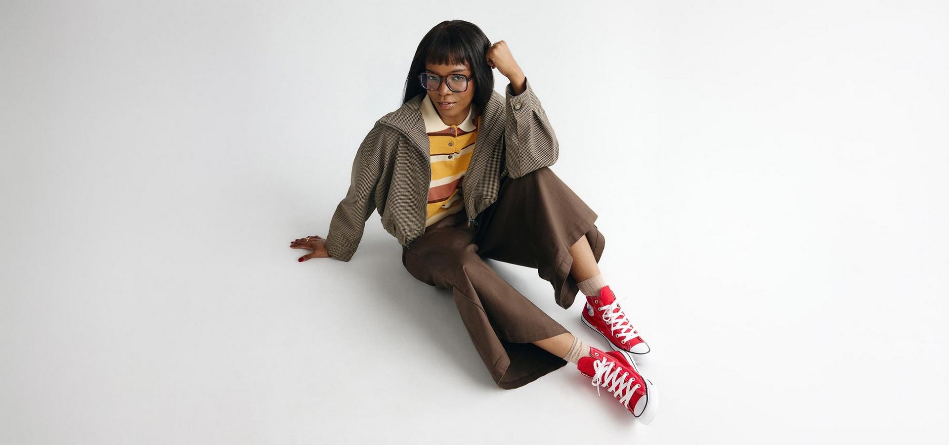 Model in braunem Herbstoutfit mit roten Canvas-Sneakern vor hellem Hintergrund