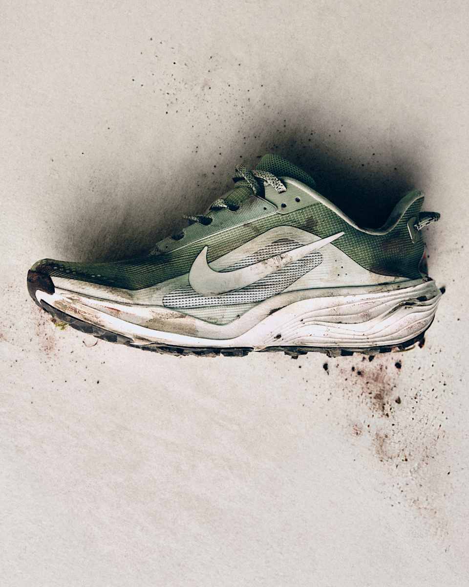 Olivgrüner Trailschuh mit Schlamm auf hellem Untergrund