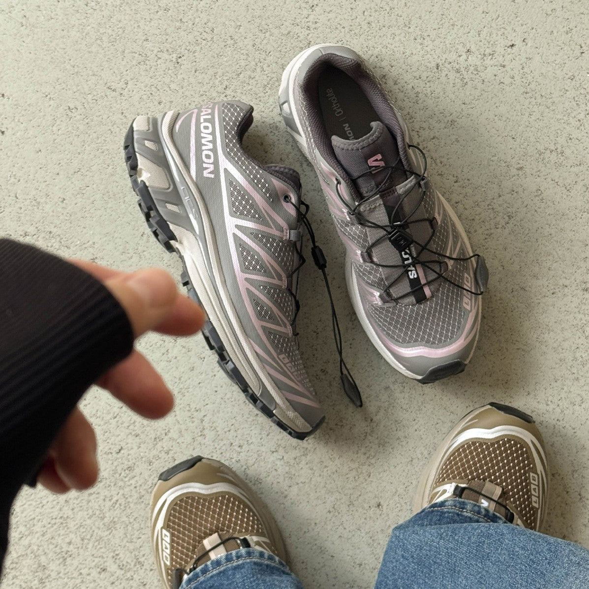 Silbergraue Trail-Sneaker neben Füßen in Jeans und beigen Sneakern