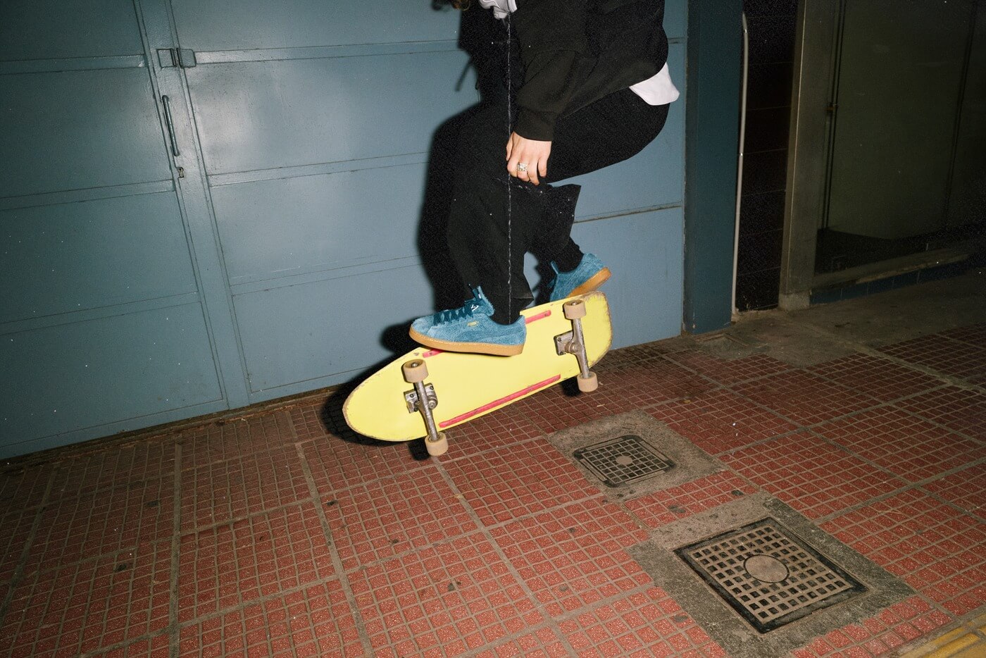 Skater auf einem gelben Skateboard in Wildleder-Sneakern vor einem Garagentor