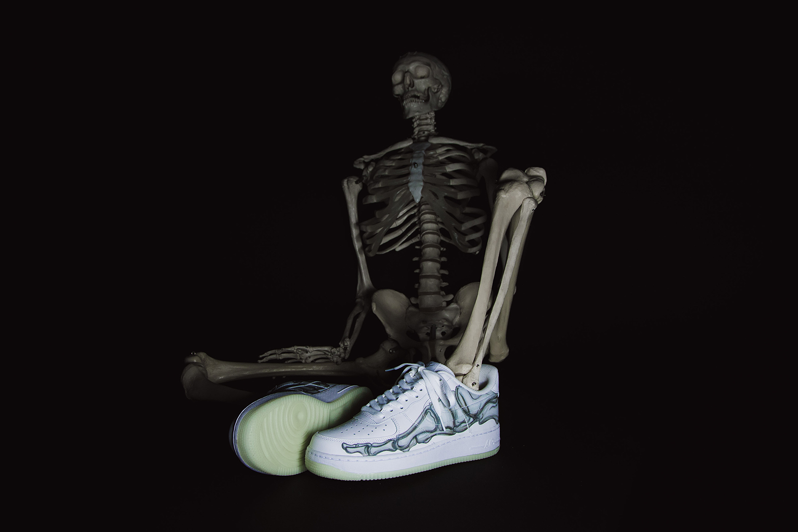 Witte Nike Air Force 1 'Skeleton' naast een skelet tegen een zwarte achtergrond